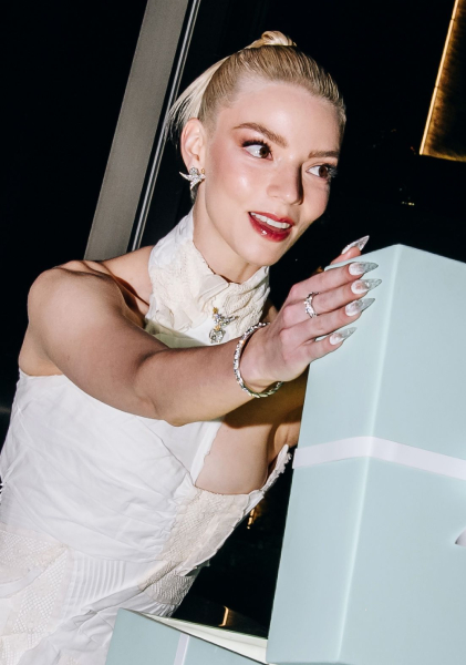 anya taylor joy in a white halter dress opening a light blue present